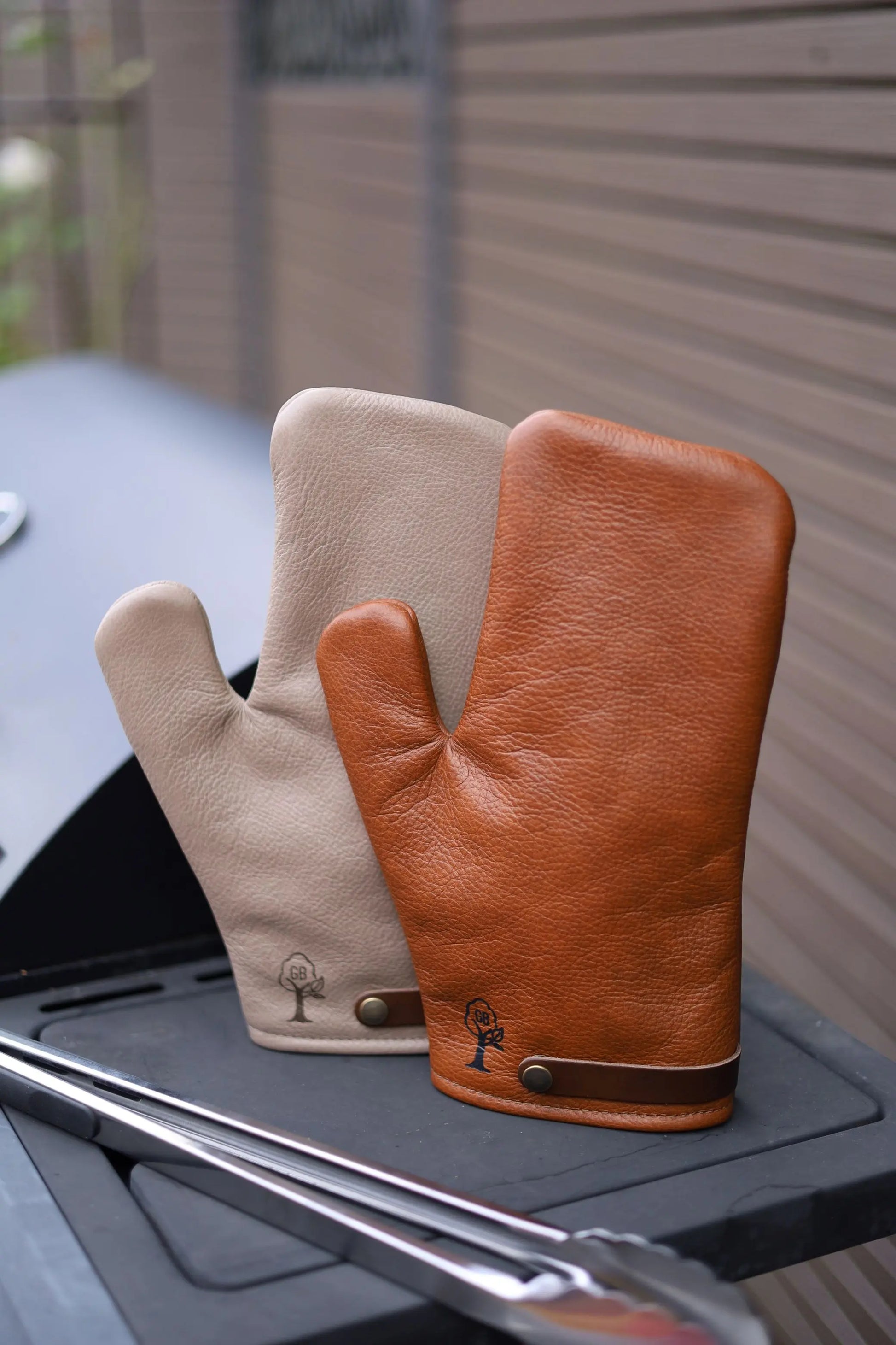 Premium Grill-Handschuh aus Leder – Whiskybraun und Smokegrau, auf einem Grill stehend
